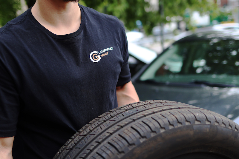 A tire storage employee in Toronto holding a tire wearing a Glenforest Garage shirt